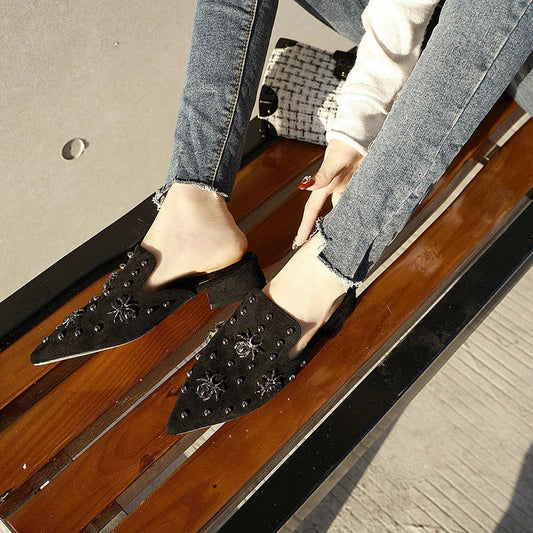 A pair of flat-bottomed, lazy half-slipper style sandals in a sleek, minimalist design with metal accents