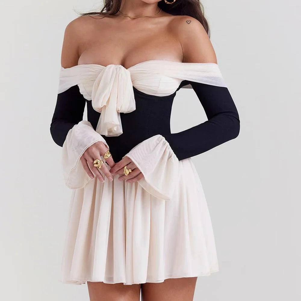 A woman wearing an elegant strapless and backless mini dress with flare sleeves, posing confidently in a party setting.