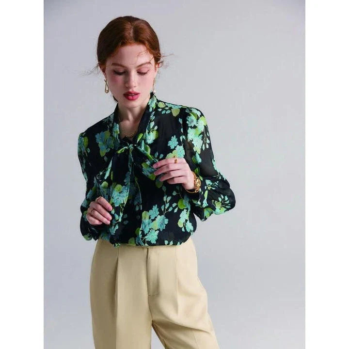 A close-up view of an elegant floral silk blend blouse with puff sleeves and a bow collar, showcasing its sophisticated British design.