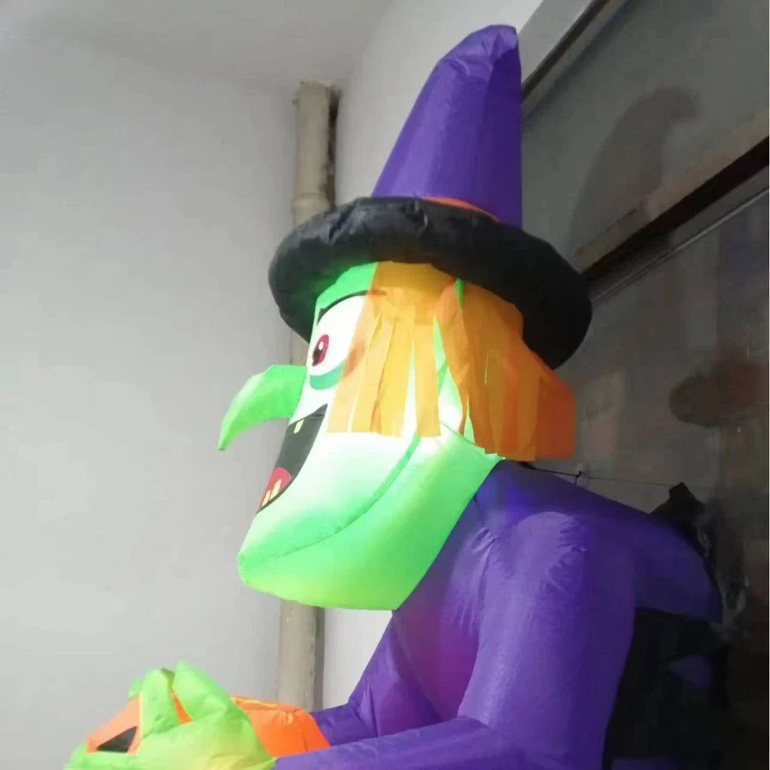 Inflatable Halloween witch decoration holding a spooky pumpkin, set up in a garden or outdoor space
