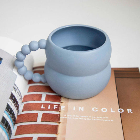 Handmade ceramic mug in beige and blue Nordic-inspired design, with a comfortable handle for enjoying hot or cold beverages.