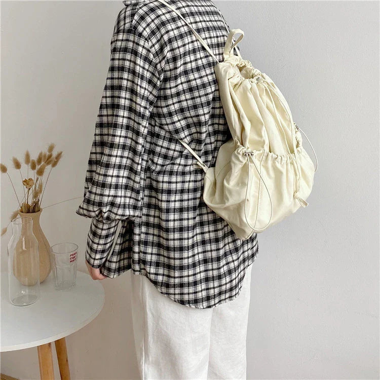 A stylish drawstring bucket bag in white, black, or brown colour options, featuring a spacious interior and adjustable closure for modern British women.
